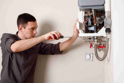 Een man die een schroevendraaier gebruikt om een cv-ketel of boiler aan de muur te repareren of te onderhouden, met het voorpaneel open om de interne onderdelen te onthullen.