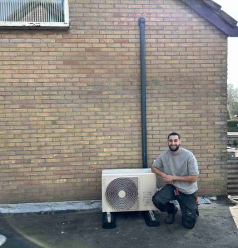Sezer Yas van Yas Installatie knielt naast een gemonteerde hybride warmtepomp bij een woning in Emmen tijdens een installatieklus.
